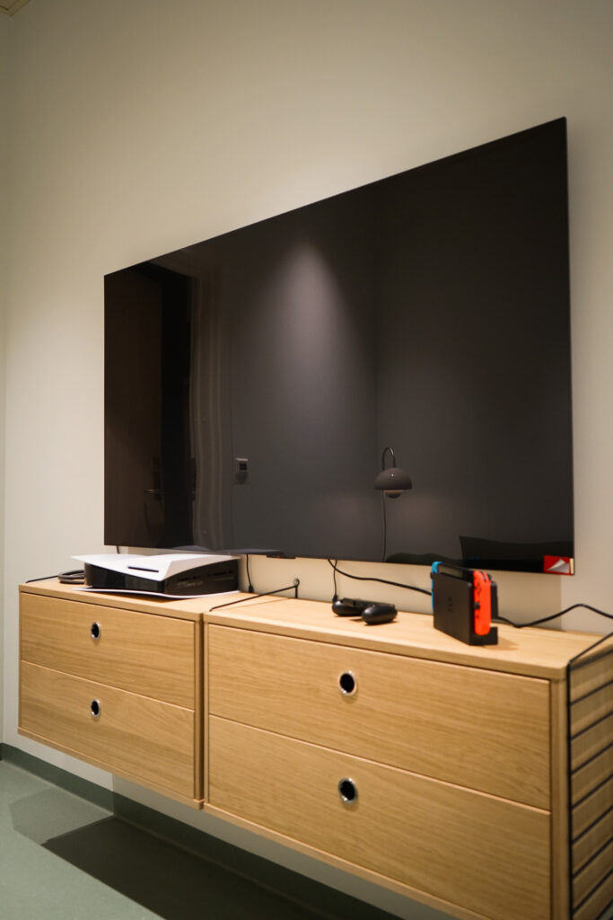 En flatskjerm-TV er montert over et treskap med en PlayStation 5, en fjernkontroll og en Nintendo Switch-konsoll på toppen.