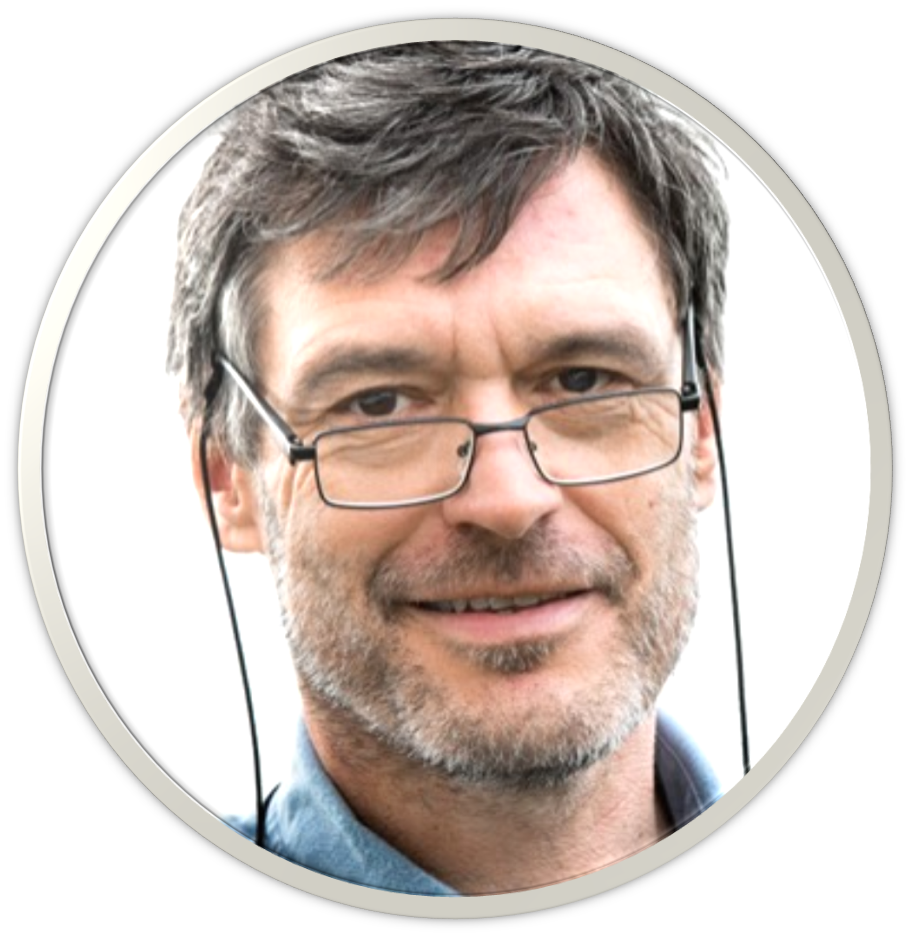 En middelaldrende mann med kort, brunt hår, briller og lyst ansiktshår, lett smilende, iført blå skjorte mot en hvit bakgrunn.