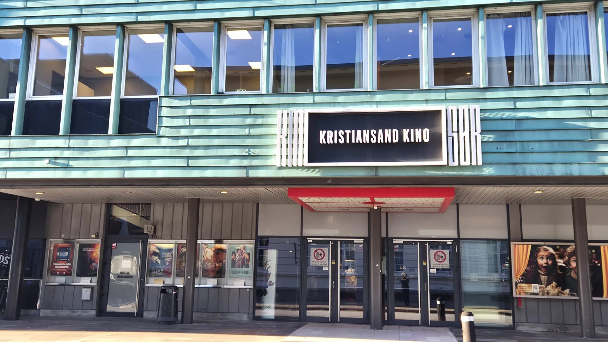 Hovedinngangen til Kristiansand Kino med store vinduer over og filmplakater ved glassdørene.