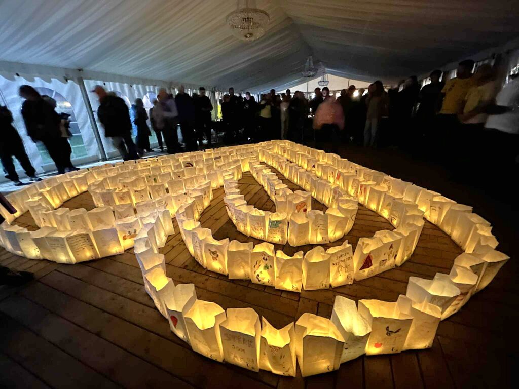 Rader av lysende papirlykter i et spiralmønster på et tregulv, mens folk står og ser på under et hvitt telt.