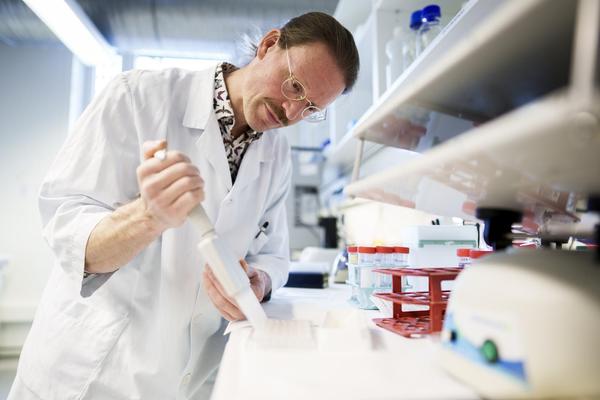 En forsker i labfrakk bruker en pipette mens han arbeider ved en laboratoriebenk med utstyr og rekvisita.