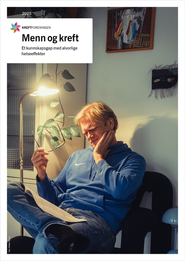En middelaldrende mann i blå genser sitter innendørs og leser i et dokument under en lampe. En plante og et innrammet bilde er synlig i bakgrunnen.