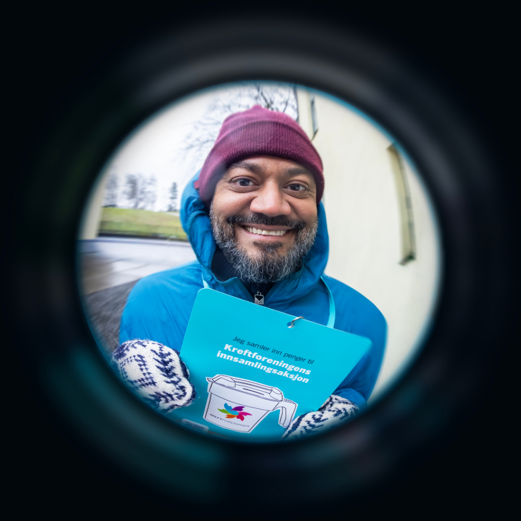 En smilende mann i rød lue og blå jakke holder innsamlerplakaten til Innsamlingsaksjonen, sett gjennom et fiskeøyeobjektiv.