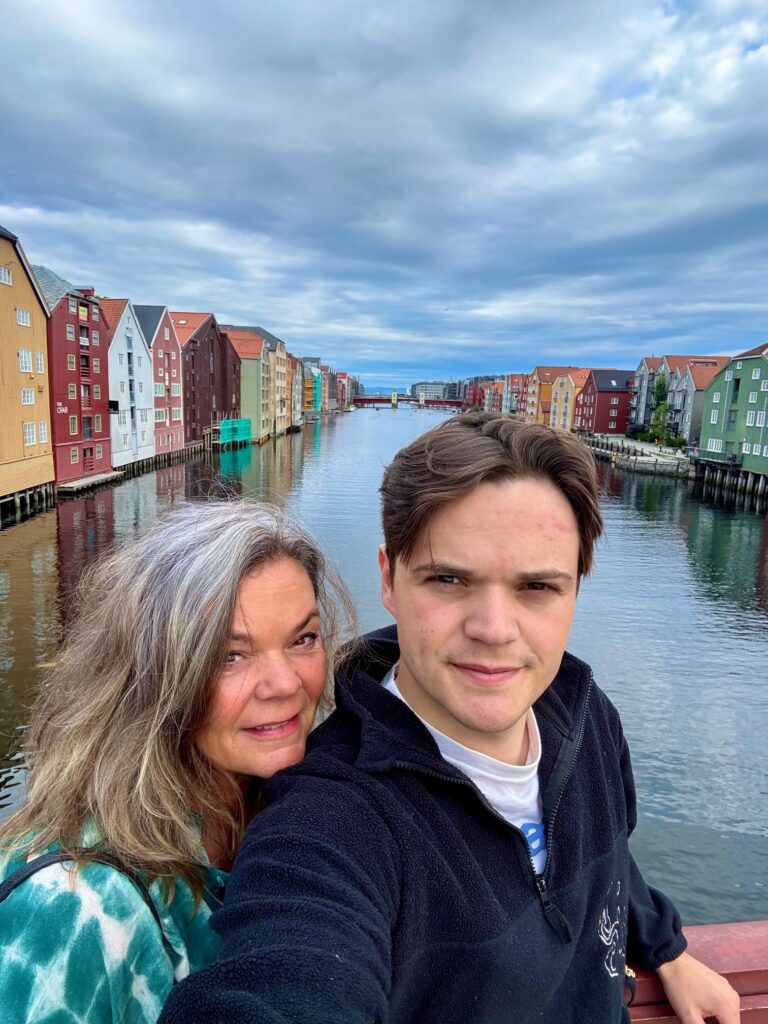 To personer står på en bro over en kanal med fargerike bygninger under en overskyet himmel.