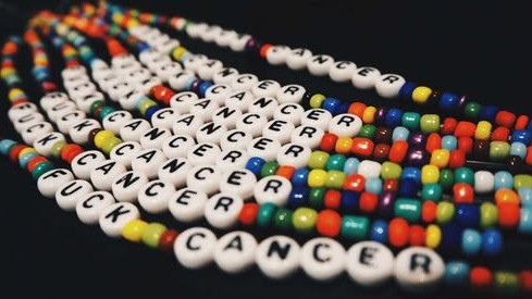 Flere fargerike perlearmbånd vises, alle med hvite perler med bokstaver som staver "FUCK CANCER".