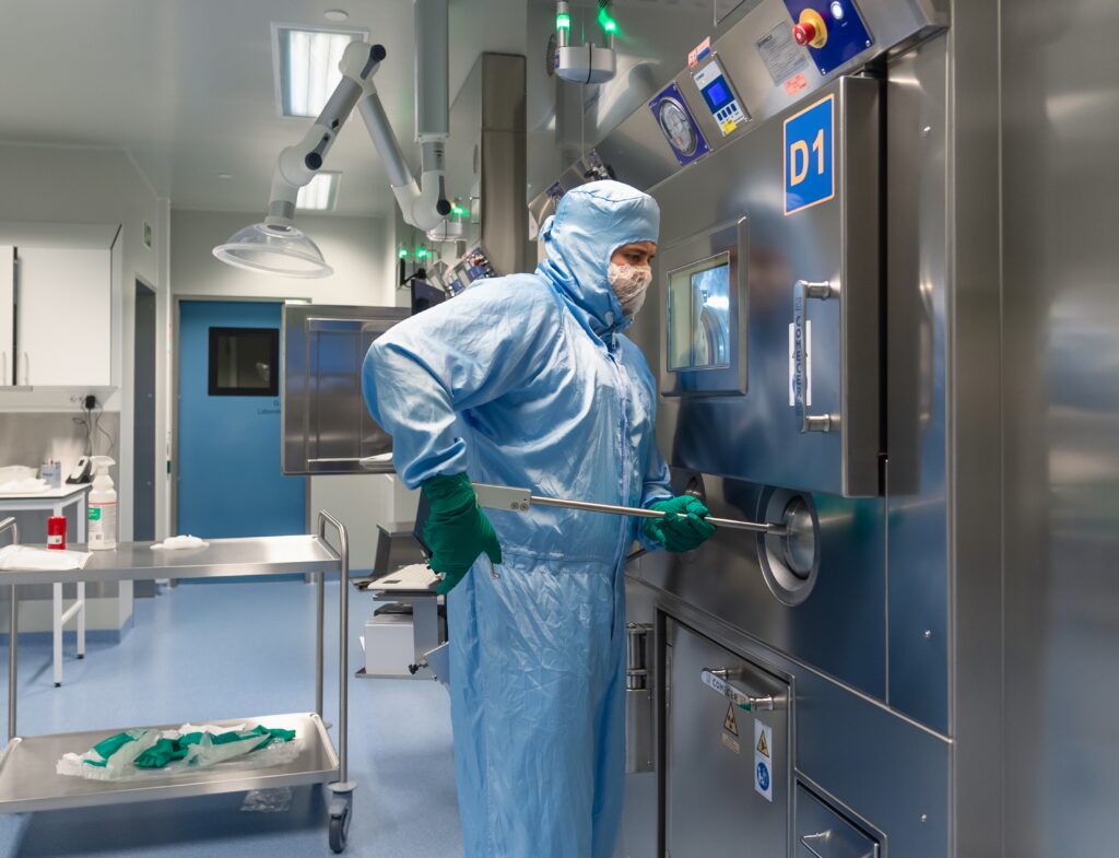 En person i fullt verneutstyr betjener utstyr inne i et sterilt laboratorium eller et renromsmiljø.