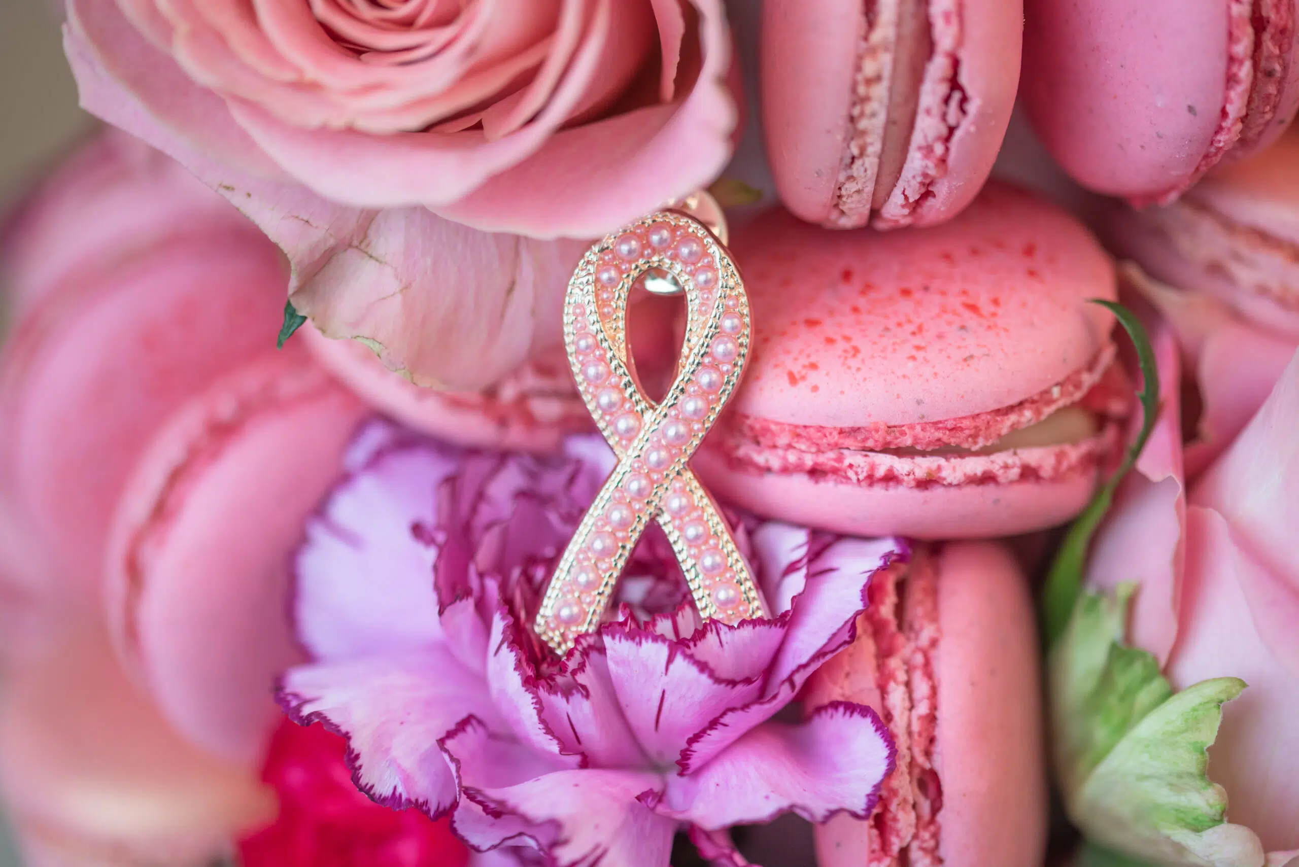 En rosa sløyfe på rosa makroner, roser og en nellike, som symboliserer oppmerksomhet rundt brystkreft.