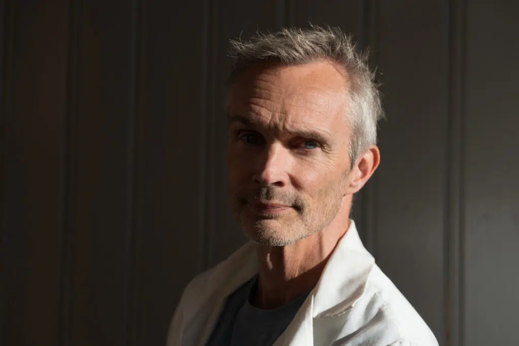 En middelaldrende mann med grått hår, kledd i en hvit skjorte med krage.