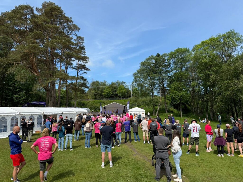 En folkemengde i en park som ser på en forestilling på en scene under et hvitt telt.