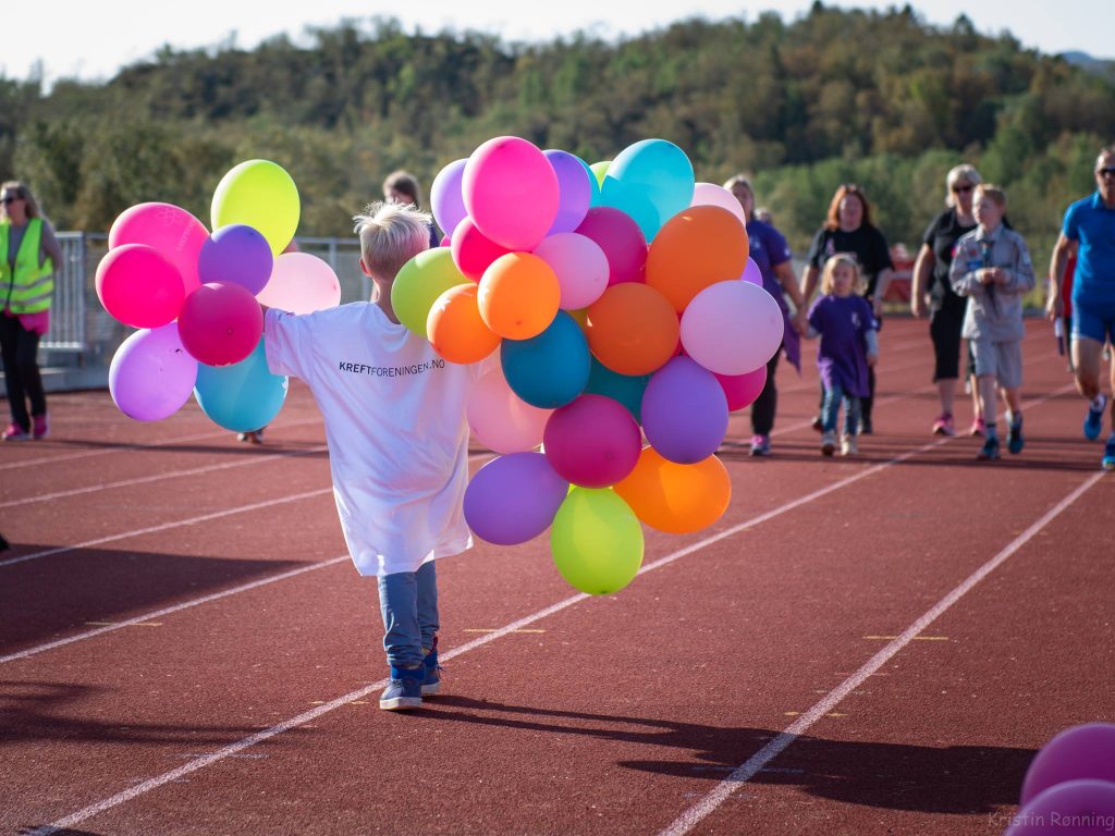 Barn med to hender fulle av ballonger i glade farger under Stafett for livet.